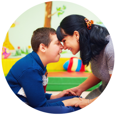 adult and child forehead to nose together holding hands on a matt in a therapy room.